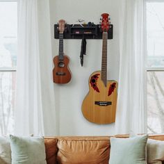 two guitars are hanging on the wall next to a couch in front of a window