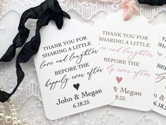 two tags with wedding names on them sitting on a lace covered tablecloth next to pearls