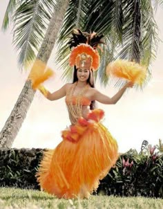 a woman in an orange dress and headdress is dancing under a palm tree