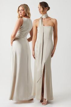 two women standing next to each other wearing dresses with high slits on the sides