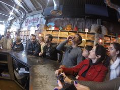 a group of people sitting at a bar in a building with shelves full of bottles