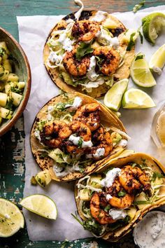 three shrimp tacos with avocado and sour cream sauce on top, next to a bowl of lime wedges