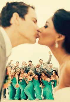 a bride and groom kissing in front of a group of people with their arms around each other