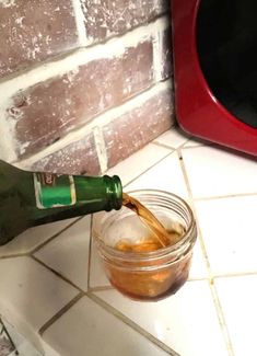 a person pouring liquid into a jar on the ground next to a microwave oven and red brick wall