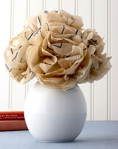 a white vase filled with paper flowers on top of a blue table next to books