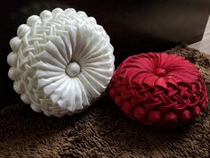 two decorative pillows sitting on top of a brown rug next to a black box with red and white designs