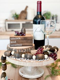 a wine bottle and some books on a table with grapes in the foreground next to a glass of wine