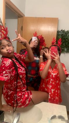 three women in red christmas pajamas taking pictures with their cell phones while sitting at a table