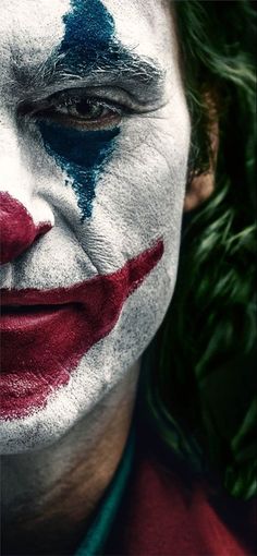 a close up of a person wearing a clown makeup and green leaves in the background