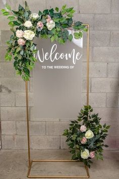 a welcome sign with flowers and greenery is displayed in front of a brick wall