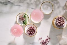 three glasses with flowers in them sitting on a marble counter top next to other glassware