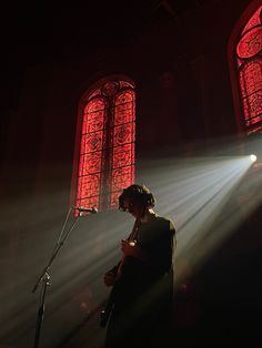 a woman standing in front of a microphone under two stained glass windows with light streaming through them