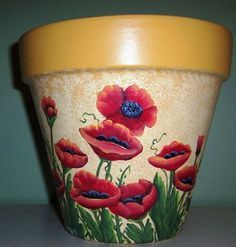 a flower pot with red flowers painted on the outside and yellow rim, sitting on a table