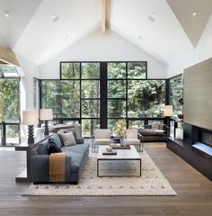 a large living room with high ceilings and floor to ceiling windows overlooking the trees outside