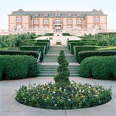 a large building with lots of plants in the front yard and stairs leading up to it