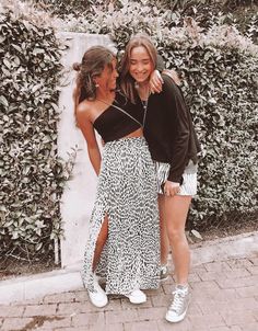 two girls standing next to each other in front of a wall covered with greenery