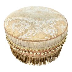 a round ottoman with tassels and gold thread work on the top, sitting on a white background