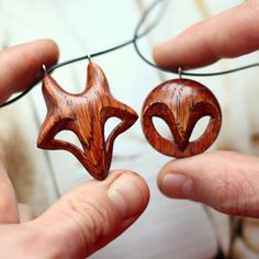 two wooden earrings are being held by someone's hands, one has a fox head on it