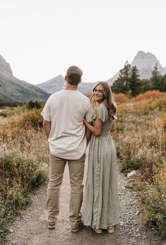 a man and woman standing on a path in the mountains looking at eachother