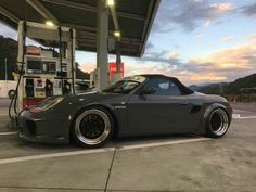 a gray sports car parked at a gas station with the sun setting in the background