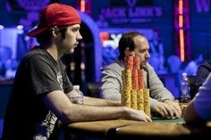 three men sitting at a table playing cards in a casino or gambling hall with neon lights behind them