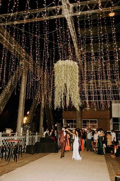 the bride and groom are dancing under string lights