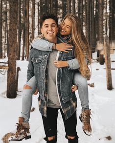 a man carrying a woman on his back through the snow in front of trees and woods