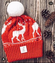 a red and white knitted hat sitting on top of a wooden table next to pine cones