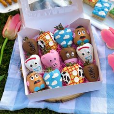 an open box filled with lots of decorated chocolates on top of a blue and white checkered table cloth