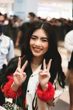 a woman with long black hair making the peace sign while standing in front of other people