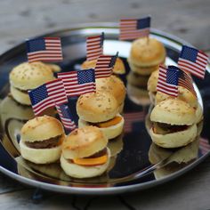 mini hamburgers with american flags on them are sitting on a plate, ready to be eaten