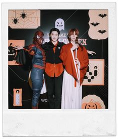 three people standing next to each other in front of a halloween themed wall with decorations