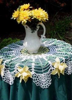 a white vase with yellow flowers sitting on top of a doily covered table cloth