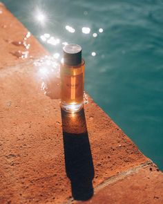 a bottle is sitting on the edge of a dock near water with its light reflecting off it's side