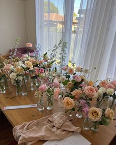 a wooden table topped with lots of glass vases filled with flowers next to a window