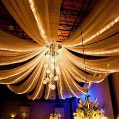 a room filled with lots of white drapes and lights hanging from the ceiling over tables