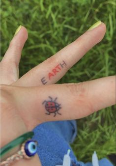 a person's hand with the word earth written on it and a ladybug tattoo