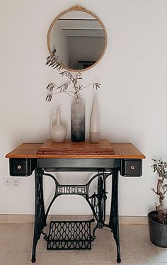 an antique sewing machine sits on a table in front of a mirror and potted plant