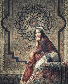 a woman sitting on top of a couch in front of a wall covered with rugs