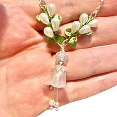 a hand holding a necklace with white flowers and green leaves on the end of it