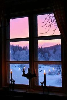 two candles are lit in front of a window with the view of snow covered mountains