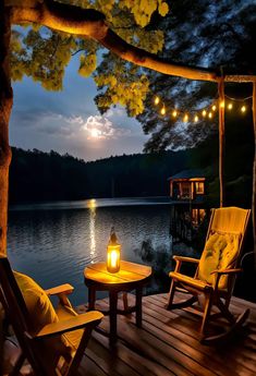 two chairs and a table on a wooden deck with lights hanging over the water at night