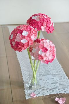 three pink and white flowers in a vase on a doily table runner with butterflies