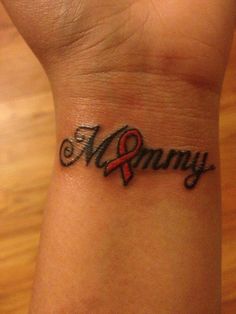 a wrist tattoo with the word mommy written in black ink on it and an orange ribbon