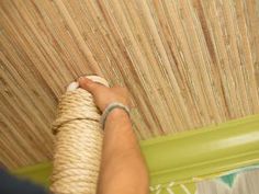 a person holding a piece of rope in front of a bamboo ceiling paneling design