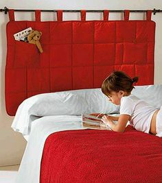 a woman laying in bed reading a book next to a red headboard with pictures on it