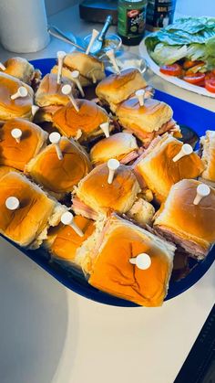 a plate full of mini sandwiches with toothpicks on them sitting on a table