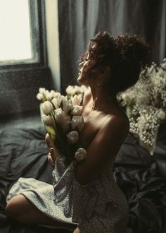 a woman sitting on a bed holding a bouquet of flowers in front of her face