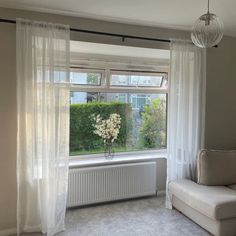 a living room filled with furniture and a window covered in white sheer curtaines next to a couch