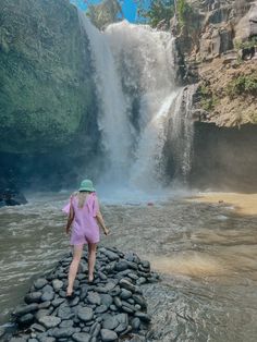 a woman standing on rocks in front of a waterfall